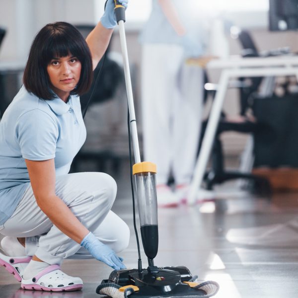 Woman uses vacuum cleaner. Group of workers clean modern office together at daytime.